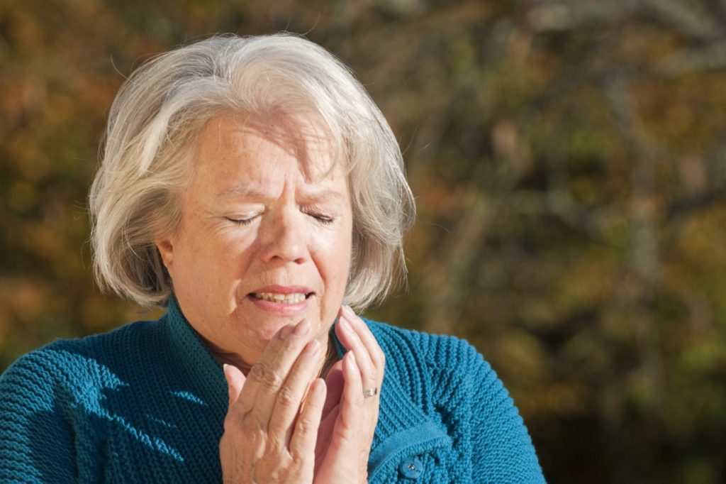 Senior woman sneezing into her hands