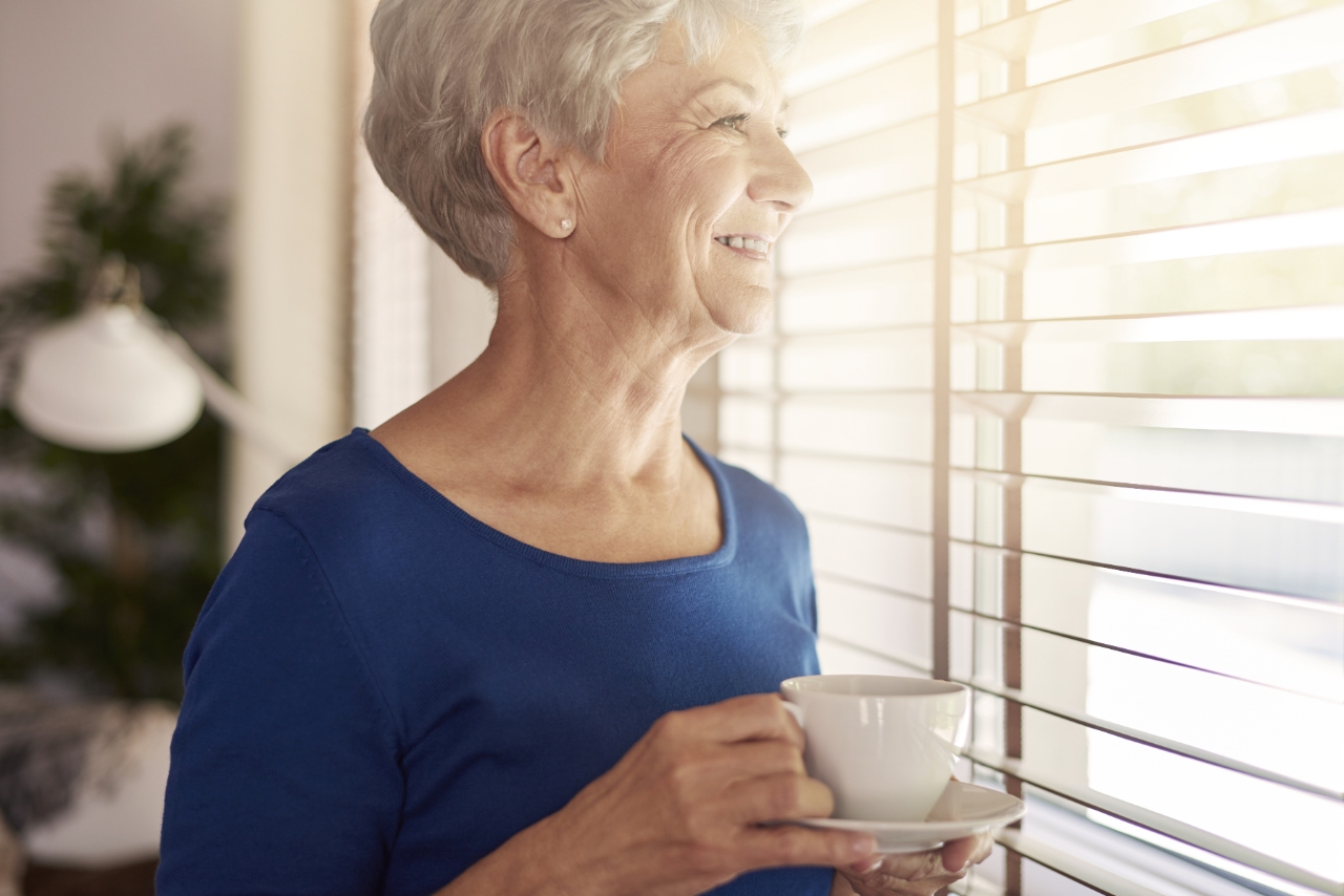 senior woman smiling looking out the window with cup of coffee